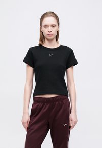 Čierne rebrované tričko s krátkymi rukávmi a okrúhlym výstrihom, na hrudi má malé biele logo Nike, v kombinácii s vínovými teplákovými nohavicami.