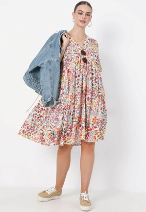 Floral dress with multicolored patterns, v-neckline, and tiered skirt. Paired with a light denim jacket and light-colored lace-up shoes.