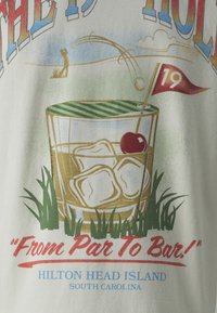 Bomull T-shirt med en grafisk design av ett glas med is och ett körsbär, en golfscen och texten: "Från Par Till Bar! Hilton Head Island."