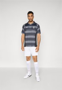 Grijze gestreepte voetbaltrui met korte mouwen, zwarte accenten en een logo. Draagt met witte shorts, witte sokken en zwart-witte voetbalschoenen.
