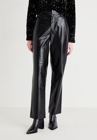Pantalons en faux cuir noir avec une texture imprimée crocodile. Design à jambe droite et taille haute, associés à des bottines noires.