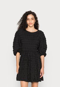 Vestido preto feito de tecido texturizado com um design franzido, apresentando mangas curtas bufantes e uma cintura elástica.