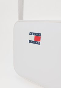 Borsa a mano rettangolare bianca con una superficie liscia, caratterizzata da un'etichetta del logo TOMMY JEANS blu e rossa sul davanti.