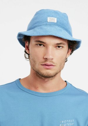 Helle blaue Bucket Hat aus strukturiertem Stoff. Beinhaltet eine flache Krone und einen breiten, nach unten geneigten Rand. Etikett auf der Vorderseite angenäht.