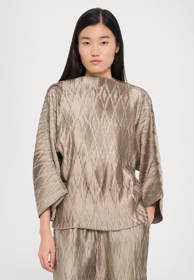 Beige pleated fabric top with a loose silhouette, wide sleeves, and textured pattern, styled with matching bottoms for a coordinated look.
