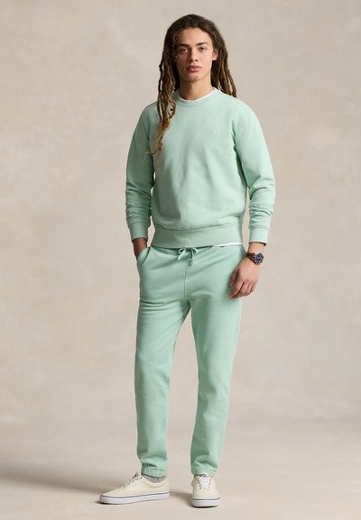 Conjunto de sweatshirt e calças de fato de treino em tecido macio de cor verde menta. Apresenta decote redondo, punhos canelados e cintura com cordão. Ténis brancos completam o visual.