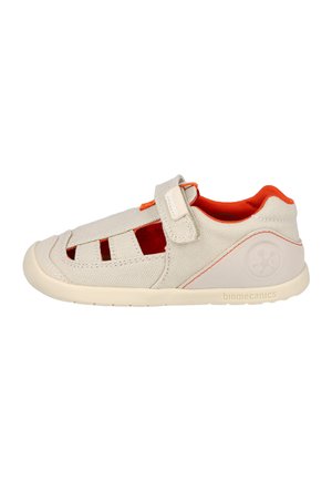 Zapato de lona beige con cortes abiertos y acentos en naranja. Cierre de tira de velcro. Suela flexible y diseño de puntera redondeada. Marca Biomecanics en el lateral.