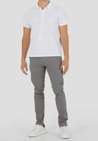 Camiseta polo blanca con tapeta, combinada con chinos grises ajustados y zapatillas blancas. Diseño simple, mangas cortas y una apariencia limpia.