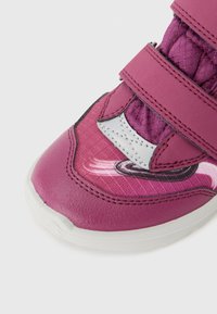 Baskets de sport violettes avec deux sangles Velcro, tige en synthétique, design texturé et un accent blanc avec un motif circulaire près de l'orteil.
