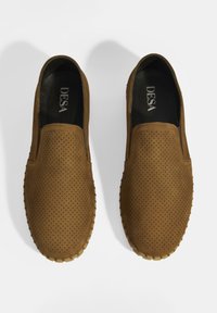 Braune Slipper aus perforiertem Wildleder mit runder Zehenpartie, strukturiertem Profil und glattem Lederinneren mit Logo.