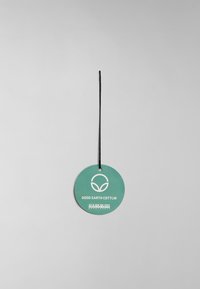 Ronde groene label met zwarte touw, met de tekst "GOOD EARTH COTTON" en een logo van drie bladeren in het wit. Gladde textuur, minimalistisch ontwerp.