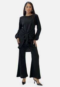 Completo due pezzi nero con top morbido con vita annodata e pantaloni a gamba larga. Tessuto liscio con maniche lunghe e tacchi a punta.