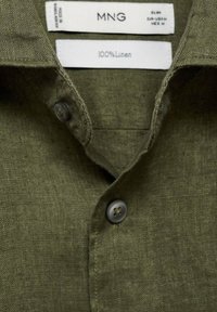 Olive green linen shirt with a collared neckline, featuring two matching buttons and textile texture visible in the fabric.