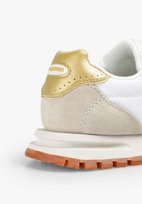 Zapatillas blancas con un talón texturizado en dorado y beige, que presentan una parte superior blanca y lisa, acentos de ante gris claro y una suela exterior naranja.
