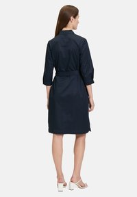 Abito blu navy con maniche a tre quarti, vita con cintura e colletto. Tessuto liscio con taglio dritto e lunghezza sopra il ginocchio.