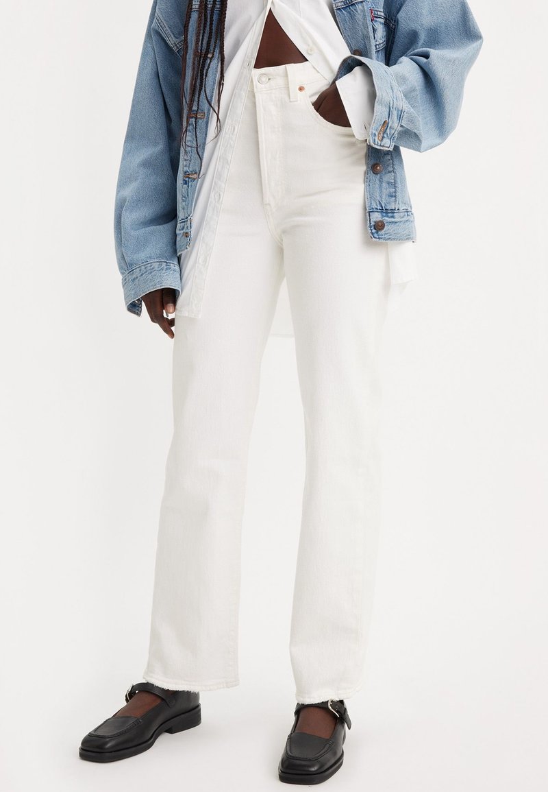 Jeans blancos de cintura alta con pierna recta, que presentan un dobladillo deshilachado. Combinados con una chaqueta de mezclilla clara y mocasines negros.