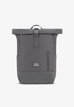 Gray canvas backpack with roll-top closure, adjustable buckle, side zip pocket, and a rubberized base for added durability. Johnny Urban branding visible.