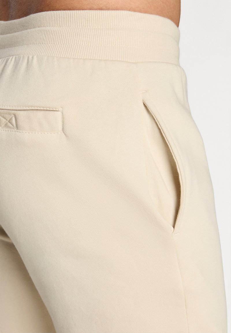 Beige Sweatpants aus strukturierter Stoffqualität, mit geripptem Bund, Seitentaschen und einem minimalistischen Design mit dezenten Steppnähten.