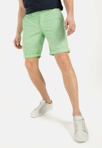 Lichtgroene opgerolde shorts met een gladde textuur, gecombineerd met witte sneakers. De outfit is casual en heeft een eenvoudig design.