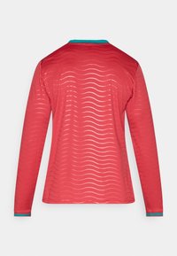 Πουκάμισο με μακριά μανίκια από κόκκινο διχτυωτό ύφασμα με κυματιστό σχέδιο, με τυρκουάζ γιακά και μανσέτες. Ο σχεδιασμός τονίζει την ελαφριά υφή.