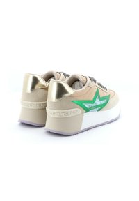 Beige suède sneakers met glanzende gouden accenten, groen sterontwerp en gemusterde veters. Dikke witte zool met paarse onderkant en decoratieve afwerking.