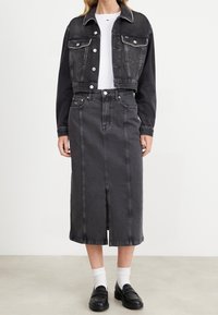 Svart denimjacka i crop-modell med silverfärgad detalj, kombinerad med en svart denimkjol med en framdelad öppning. Bärs med vita strumpor och svarta loafers.