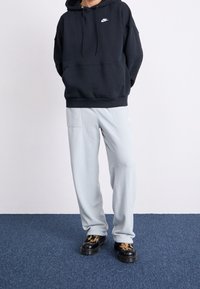 Black hooded sweatshirt with front pocket, paired with light gray fleece pants. Footwear features a patterned design and chunky soles.
