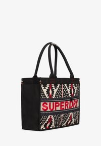 Zwarte draagtas met gevlochten etnische patronen in rood, zwart en wit; met het logo "SUPERDRY" in rode borduursels en twee stevige handvatten.