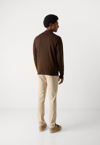 Bruine lange mouwen trui, beige chinos en tan schoenen. De trui heeft een gladde textuur en de chinos zijn aansluitend met een rechte pijp.