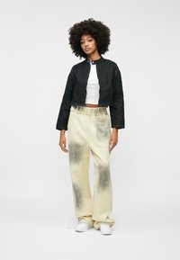 Skraćena crna traper jakna s visokim ovratnikom, nosi se preko bijelog topa bez rukava. Svijetlosmeđe hlače s tamnim mrljama i elastičnom naramenicom.