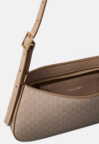 Borsa Calvin Klein realizzata in materiale beige con motivo a fantasia e texture liscia, dotata di una cerniera dorata e tracolla regolabile.