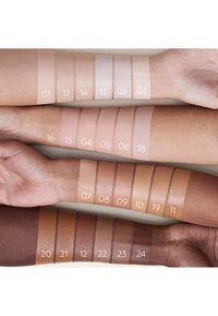 Une série d'échantillons de tons de peau sur des bras, allant du clair au foncé, avec des étiquettes numérotées pour chaque nuance. Différents tons montrent une texture lisse.