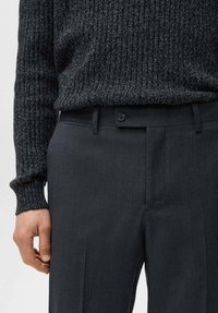 Ciemnoszare, dopasowane spodnie o gładkiej fakturze, z zapięciem na guzik, szlufkami na pasek i bocznymi kieszeniami, zestawione z ciemnym swetrem o prążkowanej fakturze.