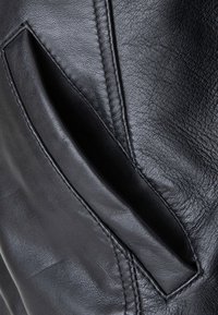 Materiale in pelle nera con una texture liscia presenta una tasca laterale. La cucitura è visibile lungo il bordo della tasca per un tocco di dettaglio in più.