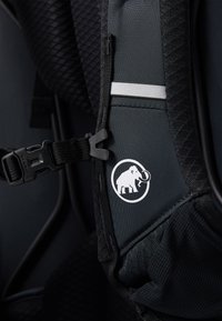 Mochila ergonómica negra con tejido texturizado, cierre lateral con hebilla y un logotipo circular blanco que representa a un elefante.