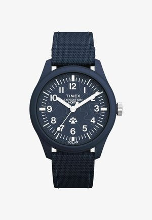 Ročna ura Timex Expedition z mornarsko modrim najlonskim pasom, okroglo številčnico, belimi oznakami ur in sončno funkcionalnostjo z teksturiranimi vzorci na številčnici.