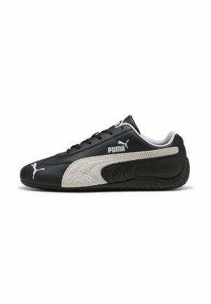 Baskets Puma noir et blanc avec profil bas, lacets noirs, logo Puma blanc sur le côté et la pointe, et bande blanche texturée sur le côté.