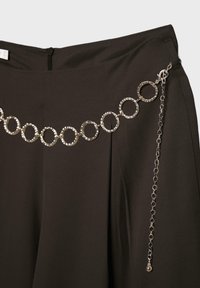 Pantalon noir à jambes larges avec une ceinture chaîne argentée composée de maillons circulaires texturés et une fermeture à pince réglable sur un fond uni.