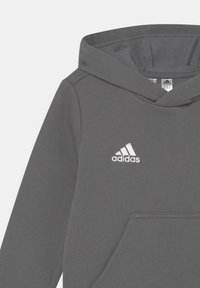Grå hettegenser laget av myk stoff med frontlomme, med en brodert hvit Adidas-logo på brystet og snøring i hetten.