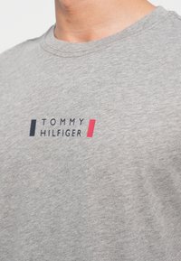 Γκρίζο βαμβακερό μπλουζάκι με το λογότυπο "TOMMY HILFIGER" σε ναυτικό μπλε και κόκκινο. Στρογγυλή λαιμόκοψη και κοντά μανίκια, με λεία υφή.