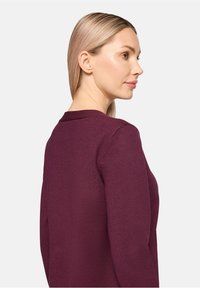 Bordowy sweter z okrągłym dekoltem, dopasowanymi rękawami i gładką dzianiną. Widok z boku podkreśla czyste linie i minimalistyczny design.