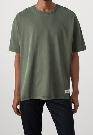 Dunkelolivgrünes Baumwoll-T-Shirt mit lässigem Schnitt, Rundhalsausschnitt und kurzen Ärmeln. Verfügt über ein dezentes Markenlabel am Saum.