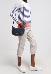 Sweter w paski w bieli i granacie z koralowymi akcentami; jasnobeżowe spodnie typu cropped; czarna torebka na ramię; białe trampki na platformie.