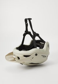 Cască de bicicletă off-white cu curele ajustabile negre, deschideri pentru ventilație și protecție pentru bărbie. Logo notabil pe lateral. Material din plastic neted.