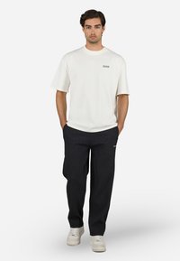 Hvid bomulds t-shirt med korte ærmer og rund halsudskæring, parret med sorte ribbede bukser og lyse sneakers.