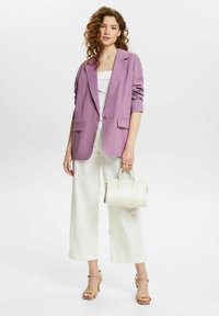 Blazer en lavande avec revers notch, deux poches avant, assorti à un pantalon large blanc et un petit sac à main blanc. Talons réglables neutres.