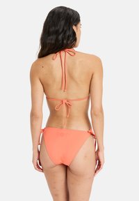 Korall bikini szett, nyakba akasztható dizájnnal. Kötött pántokkal és Roxy logóval a bugyi hátulján. Simaszerkezet.