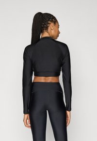 Μαύρο crop top με μακριά μανίκια, εφαρμοστή σχεδίαση και λεία υφή, σε συνδυασμό με μαύρο ψηλόμεσο κολάν που διαθέτει ζώνη χωρίς ραφές.