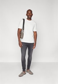 Weißes Kurzarm-T-Shirt, graue Slim-Fit-Jeans und graue Slipper. Eine schwarze Umhängetasche schafft einen Kontrast mit einem schlanken Design.