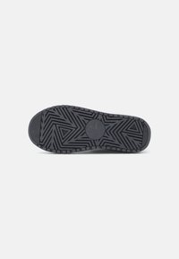 Zwarte rubberen schoenen zool met een geometrisch profielpatroon, met een cirkelvormig logo in het midden en variërende texturen langs de randen.